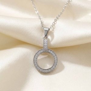 گردنبندجواهرات نقره‌ای رنگ با طرح دو حلقه متصل به هم نگین‌دار که روی پارچه حریر روشن قرار گرفته است