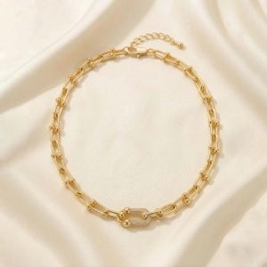 گردنبد طلایی با طرح زنجیر U شکل (مدل تیفانی) و حلقه‌های مرکزی نگین‌دار، قرار گرفته روی پارچه حریر روشن