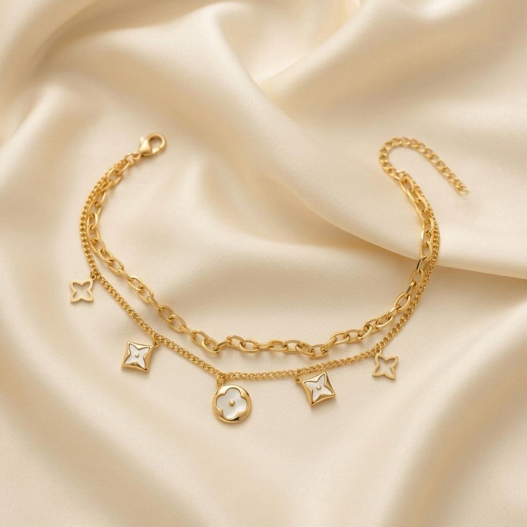Gold-Layered-Clover-Charm-Bracelet دستبند زنانه دو زنجیره طلایی رنگ با آویزهای طرح گل شبدر صدفی و توخالی، روی پارچه ساتن کرم رنگ