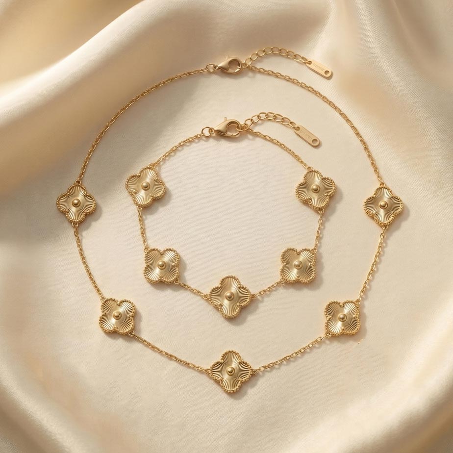 Van-Cleef-style-golden-two-piece-set-bracelet-and-necklace-with-a-sunburst-design ست دو تکه زیورآلات طلایی رنگ شامل یک گردنبند با پنج پلاک شبدر و یک دستبند با پنج پلاک مشابه. سطح پلاکهای این ست دو تکه طرح ون کلیف طلایی دارای خطوط شیاردار و بافت خورشیدی است که روی یک پارچه ساتن کرم رنگ قرار گرفتهاند.