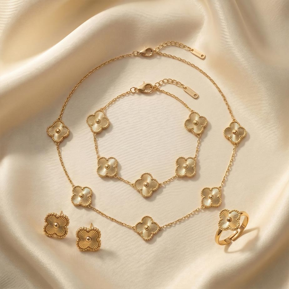 gold-jewelry-set-van-cleef-sunburst-texture سرویس کامل طرح ون کلیف بافت خورشیدی به رنگ طلایی روی پارچه ساتن شامل گردنبند پنج گل، دستبند، یک جفت گوشواره میخی و انگشتر که همگی دارای حاشیه نقطهکوب هستند.