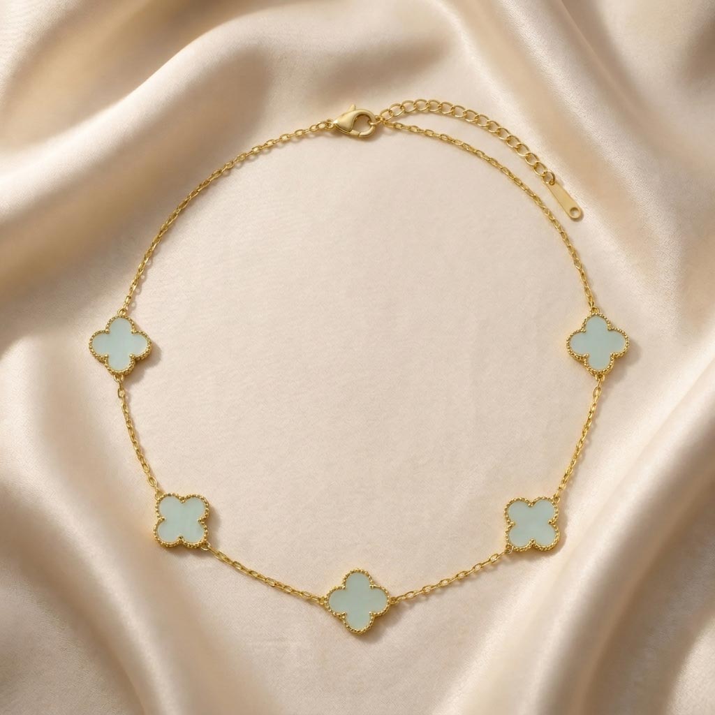 gold-van-cleef-tiffany-blue-necklace تصویر گردنبند طلایی طرح ون کلیف نگین آبی تیفانی با پنج پلاک به شکل گل شبدر که روی یک پارچه ساتن روشن قرار گرفته است.