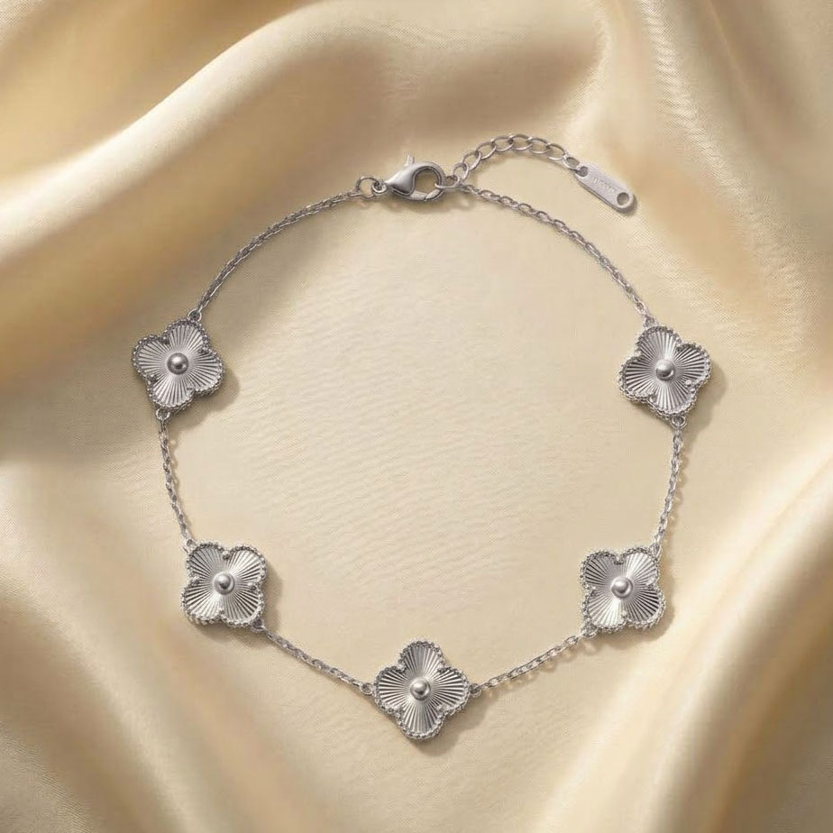 silver-five-clover-bracelet یک دستبند زنجیری ظریف با پنج پلاک به شکل گل شبدر چهار برگ روی پارچه ابریشمی کرم رنگ، که نمایانگر جزئیات و ظرافت یک دستبند طرح ون کلیف نقرهای است.