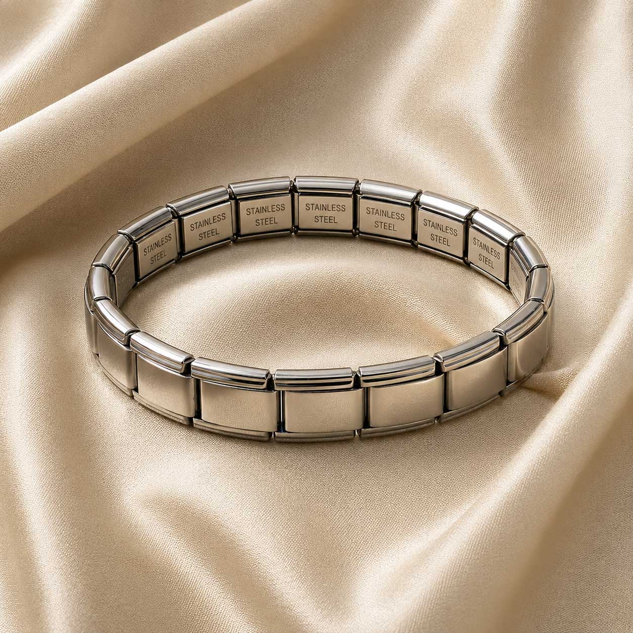 silver-italian-nomination-style-bracelet دستبند نقرهای طرح نومینیشن ایتالیایی با قطعات مستطیلی استیل براق که روی یک پارچه ابریشمی کرم رنگ قرار گرفته است.
